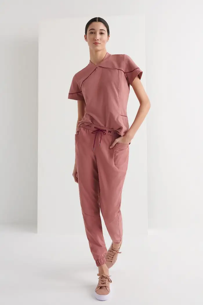 Casacas para farmacia en Las Palmas de diseño moderno. Mujer luciendo camisola sanitaria rosa empolvado con cuello asimétrico y pantalón jogger.