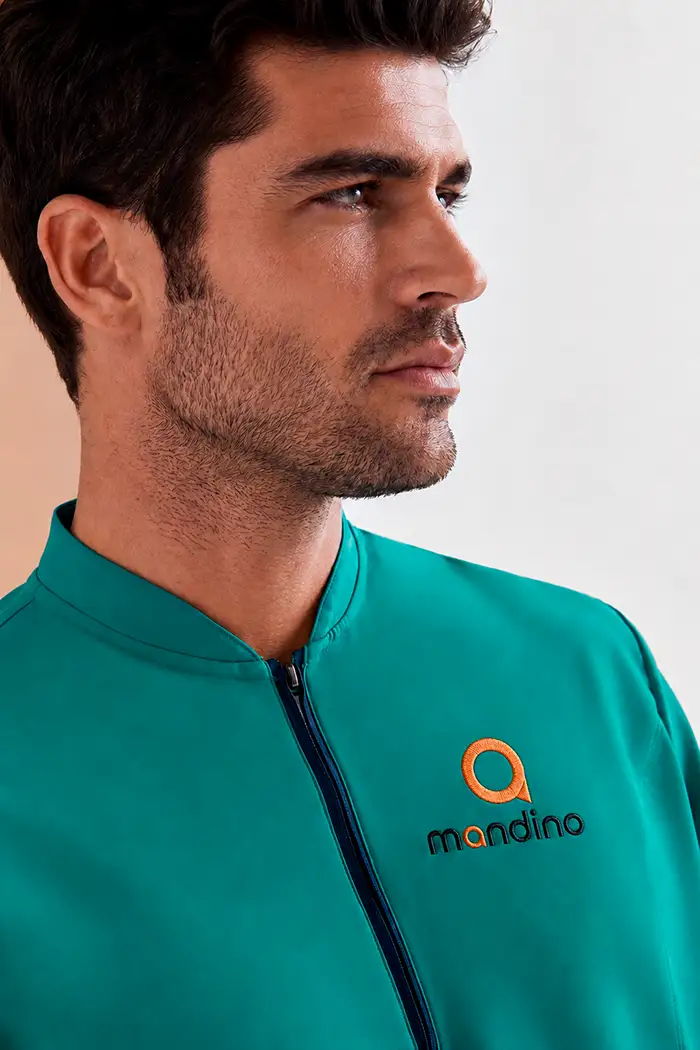 Personalización de uniformes de farmacia con bordado corporativo. Detalle de logotipo bordado sobre el pecho de una casaca sanitaria verde esmeralda.