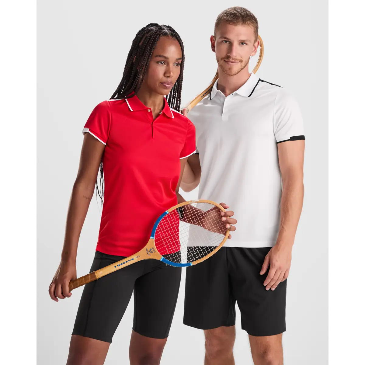 Polo técnico bicolor Roly TAMIL 24 Polo Roly TAMIL en blanco y negro, junto a un polo femenino rojo, vista frontal